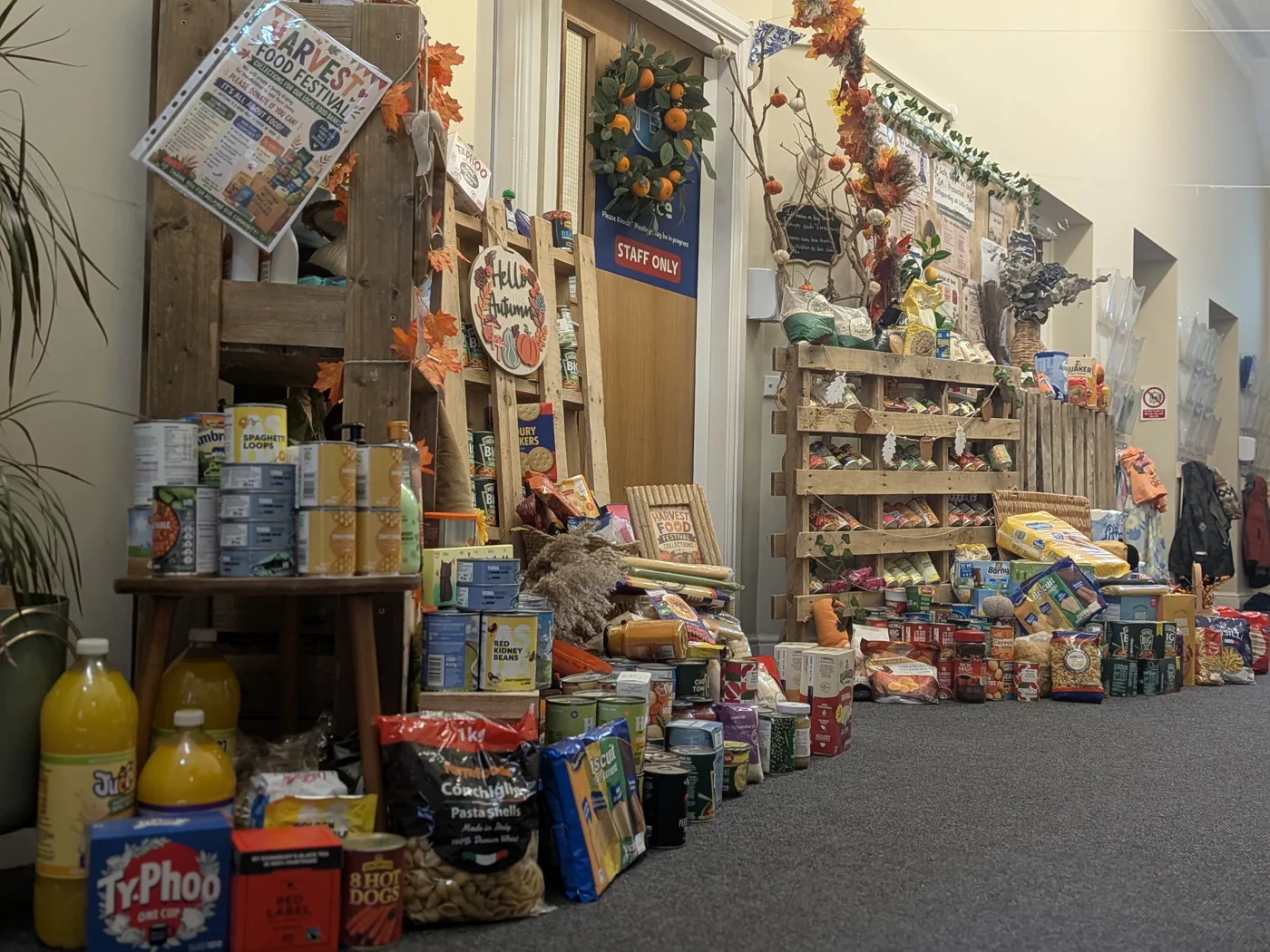 Wooden crates and shelves stacked with tins, packets, cereal and juice along a nursery corridor, with autumn decorations