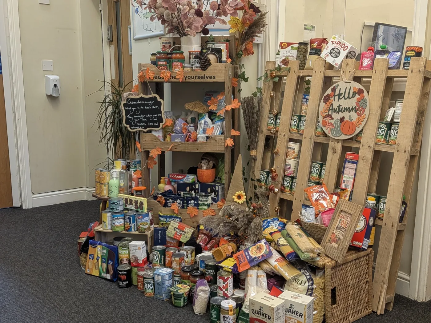 Wooden pallet shelving piled with tins, jars and dried food, decorated with pumpkins and autumn leaves