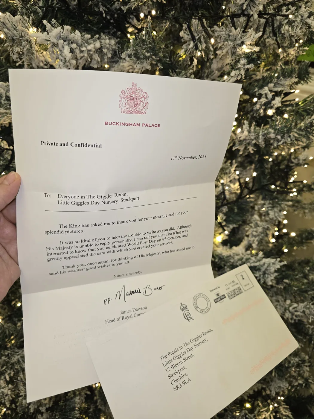 A letter on Buckingham Palace notepaper dated 11 November 2025, addressed to Everyone in The Giggler Room, Little Giggles Day Nursery, Stockport, held up in front of a Christmas tree
