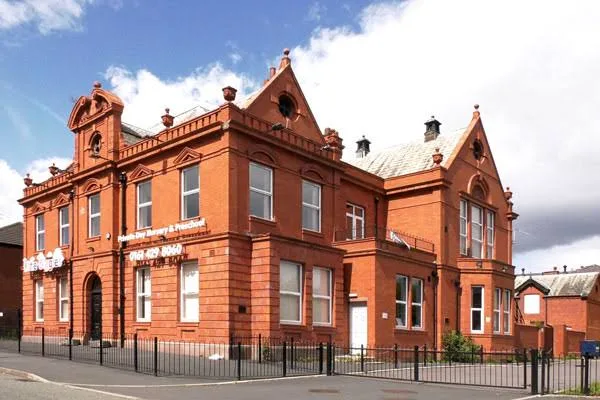A large red-brick Victorian building with gables and railings on a street corner