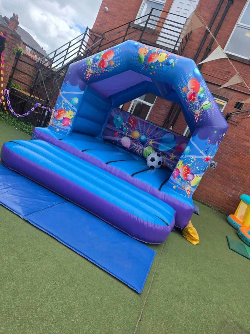 A blue and purple bouncy castle on artificial grass in the nursery garden
