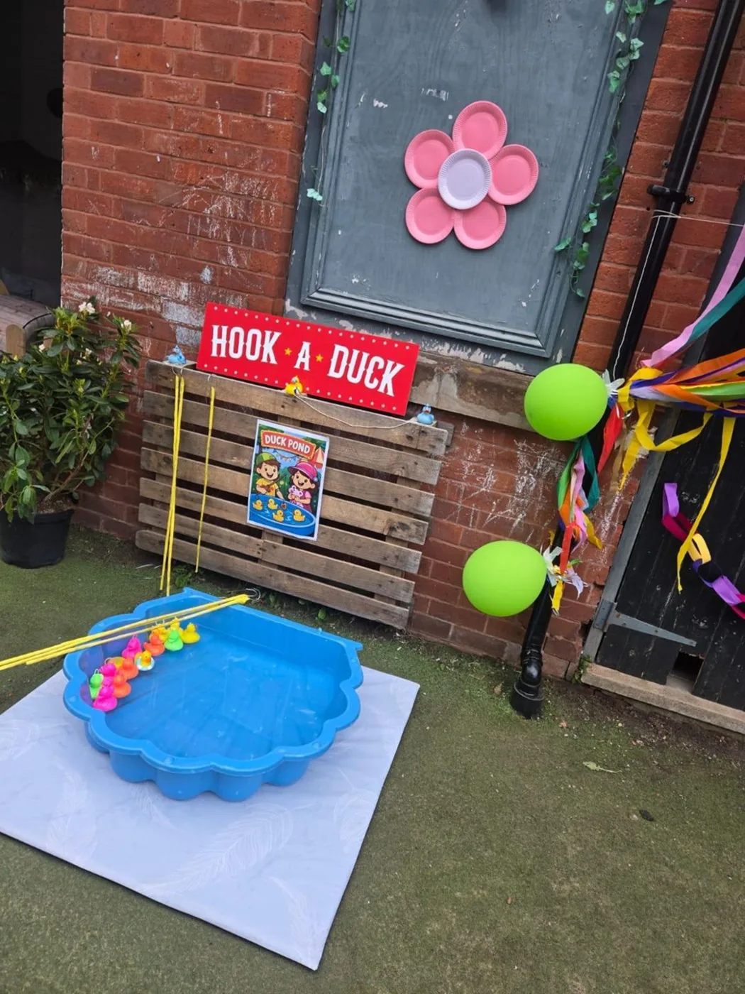 A Hook-a-Duck sign above a blue paddling pool of plastic ducks, with balloons tied to a wooden pallet