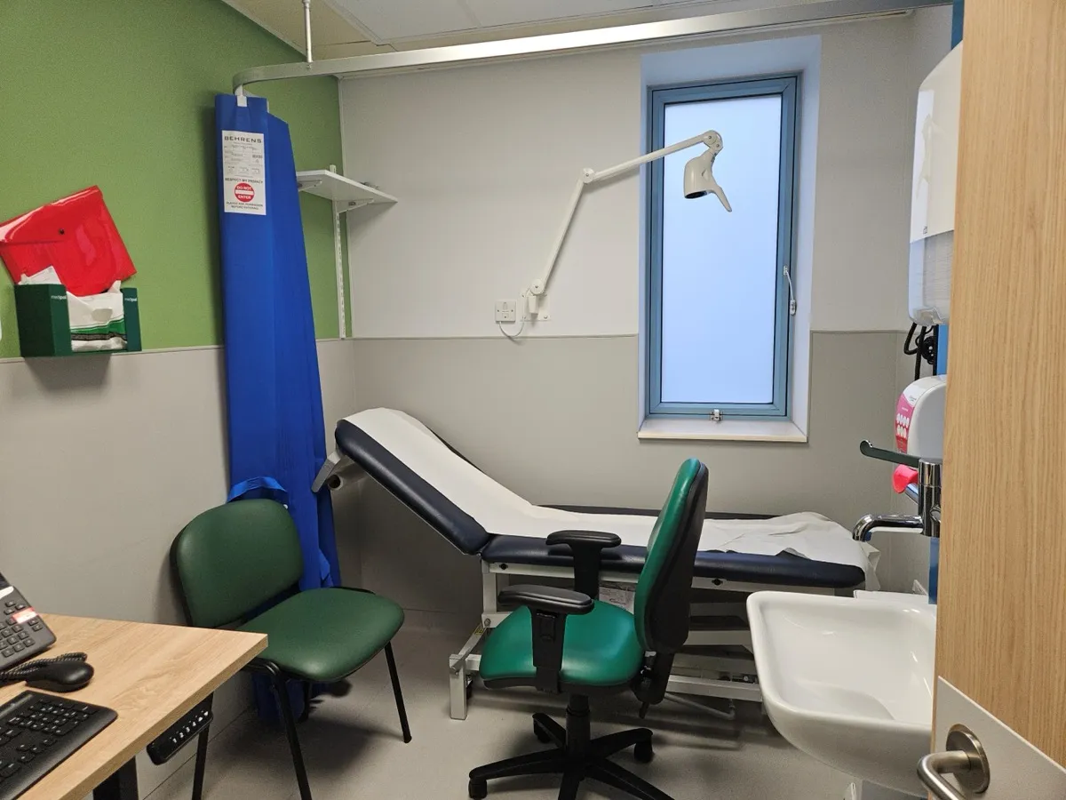 A consultation room in the new urgent treatment centre at Stepping Hill Hospital, with an examination couch, a curtain, a sink, a desk with a computer and two green chairs